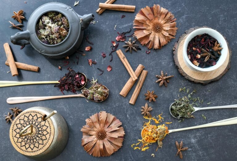 A flat lay of various herbal tea ingredients, spices, and rustic utensils on dark surface.